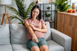 Mid-adult pregnant Asian woman having a rash (skin condition) while sitting on the sofa at home.